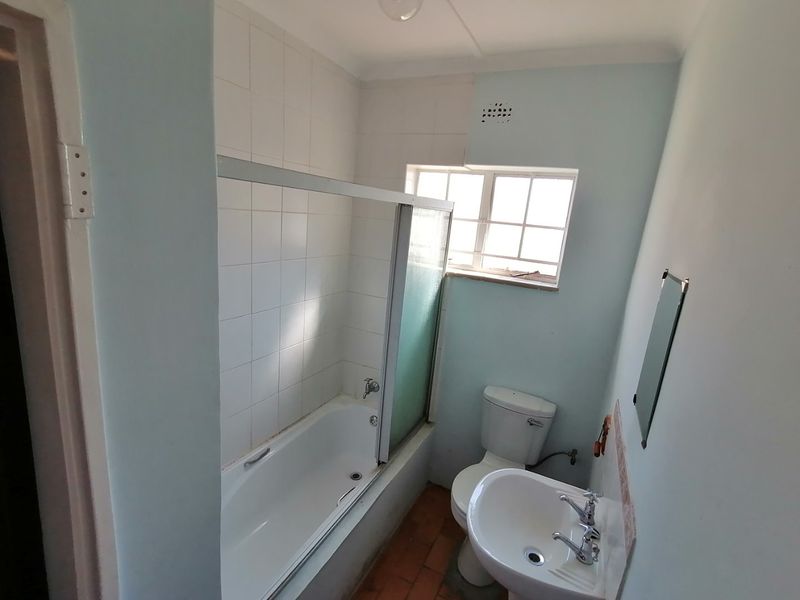 A functional bathroom featuring a bathtub with a shower screen, a pedestal basin, and a toilet, requiring cosmetic updates to modernize the space.