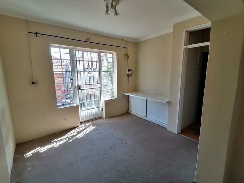 An empty living area featuring a security gate, burglar bars, and built-in shelving, requiring cosmetic updates to improve its overall appeal.
