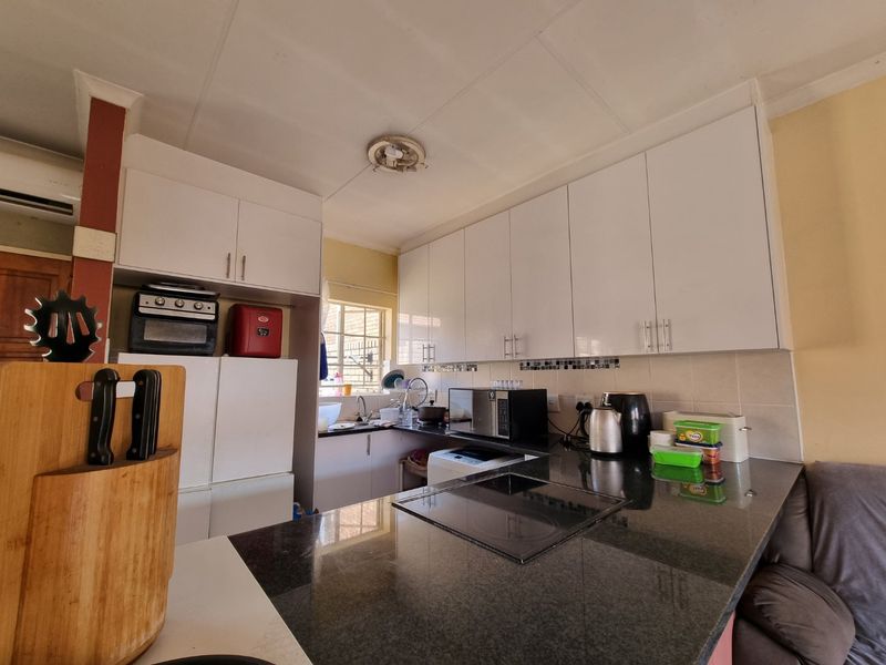 Functional kitchen featuring white cabinetry, dark granite countertops, integrated hob and oven, and a tiled backsplash with a practical layout.