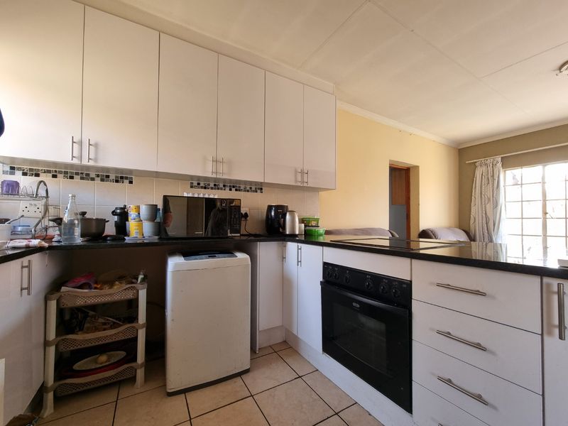 A functional kitchen featuring white cabinetry, granite countertops, built-in oven and hob, and tiled flooring, offering a practical layout for daily meal preparation.