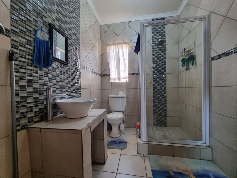 A functional bathroom featuring a tiled vanity with a vessel sink, a separate shower enclosure, and mosaic tile accents.