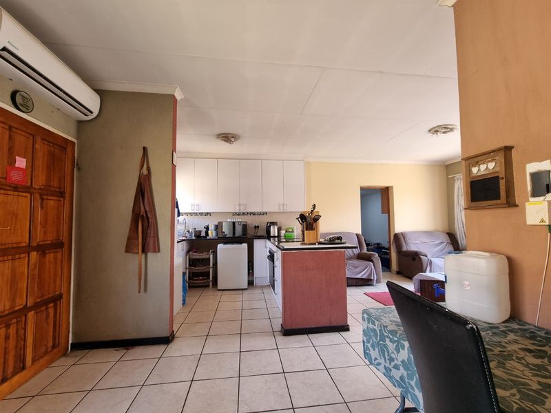 Open-plan living and kitchen area featuring tiled flooring, white cabinetry, a central kitchen island, and a wall-mounted air conditioning unit.