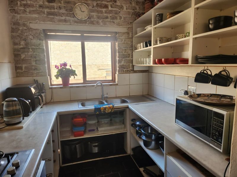 A functional kitchen featuring an exposed brick wall, open shelving, double bowl sink, and tiled splashback with a practical U-shaped layout.