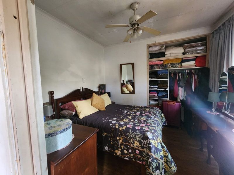 A bedroom featuring timber flooring, a ceiling fan, and built-in wardrobe storage. The room requires cosmetic updates to the ceiling and wall finishes.