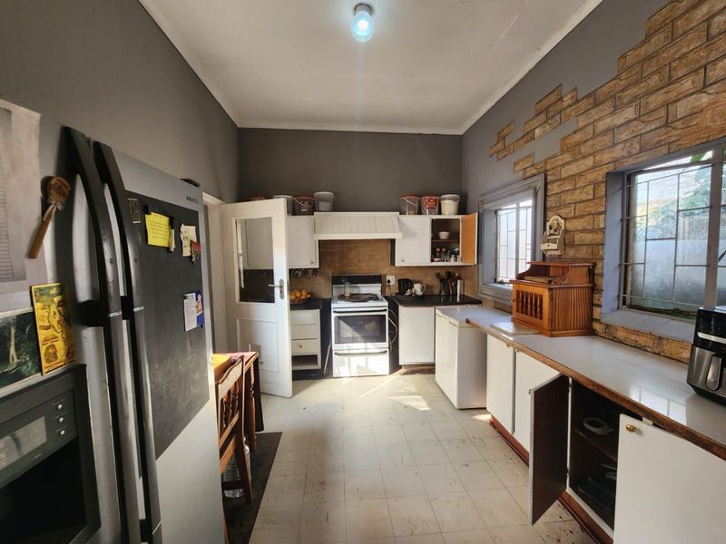 A dated kitchen featuring built-in cabinetry, a freestanding stove, and an exposed brick feature wall, requiring cosmetic updates to modernize the space.