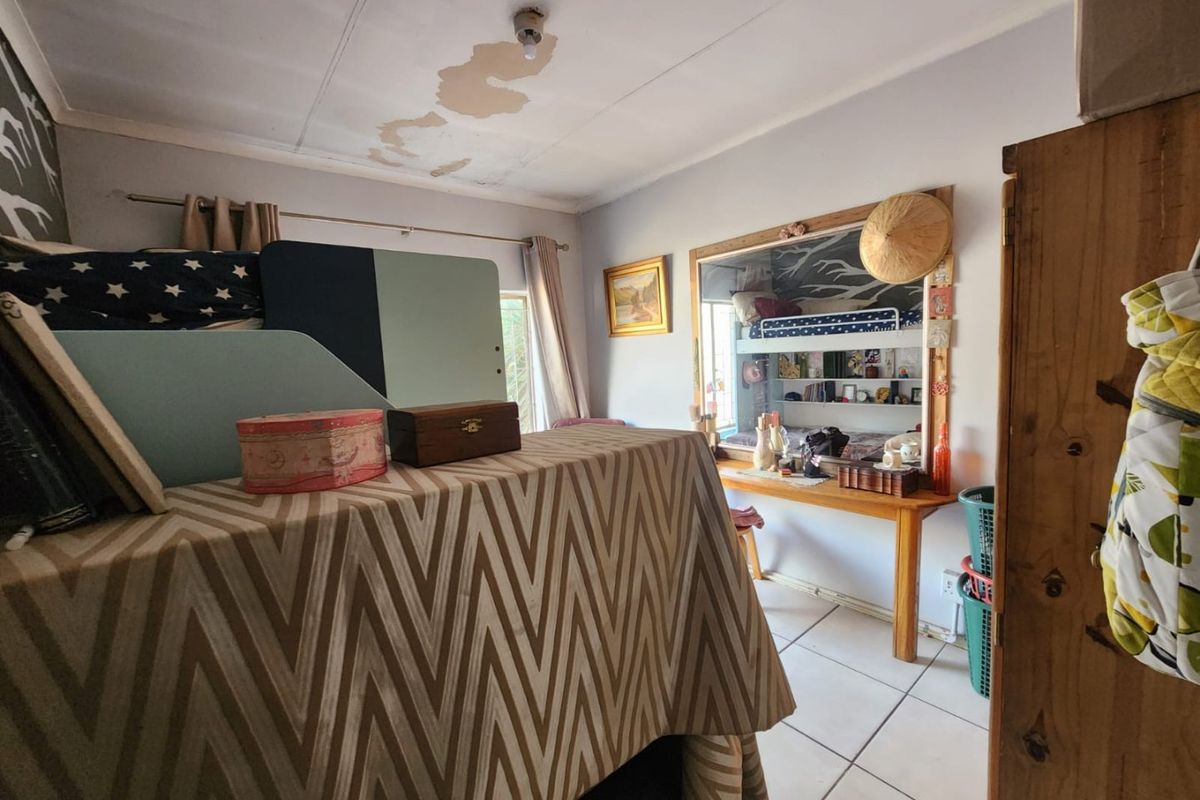 A bedroom featuring tiled flooring, a built-in desk, and integrated shelving, currently showing signs of ceiling water damage and peeling paint.