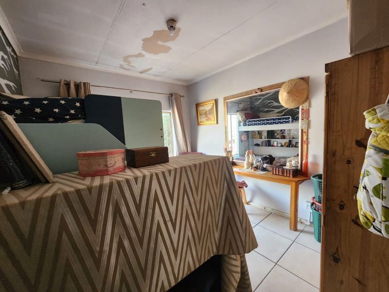 A bedroom featuring tiled flooring, a built-in desk, and integrated shelving, currently showing signs of ceiling water damage and peeling paint.