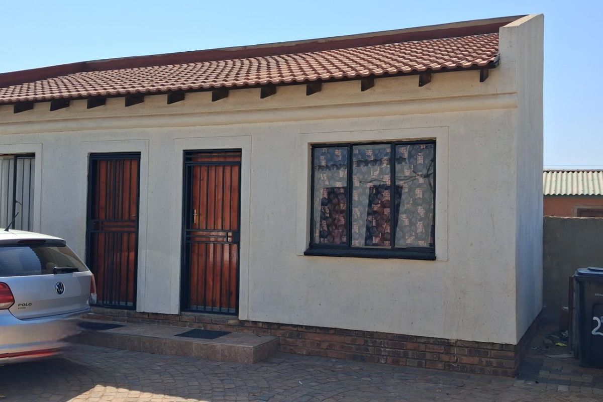 Front elevation of a single-story residential house featuring a terracotta tiled roof, security gates, and a paved driveway area.