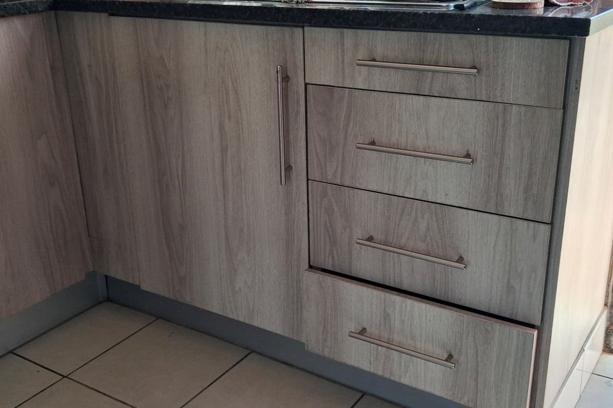 A close-up view of kitchen cabinetry featuring wood-look laminate doors, drawers with metal handles, and a dark granite countertop.