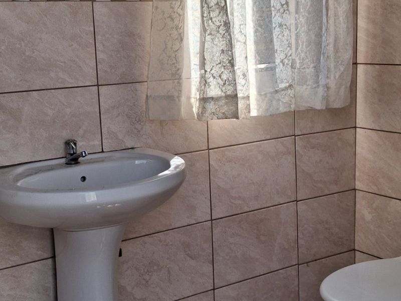 A functional bathroom featuring a pedestal basin, toilet, and neutral ceramic wall and floor tiling.