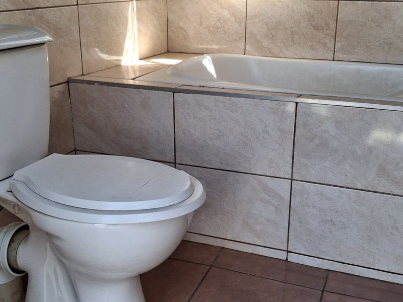 A functional bathroom featuring a standard ceramic toilet and a built-in bathtub with neutral wall and floor tiling.
