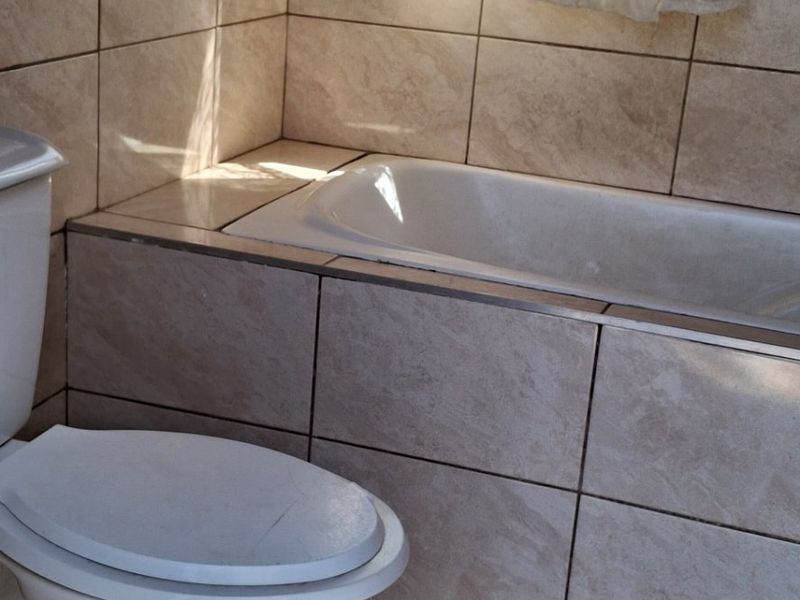 A functional bathroom featuring a built-in bathtub, ceramic wall and floor tiling, and a standard toilet.