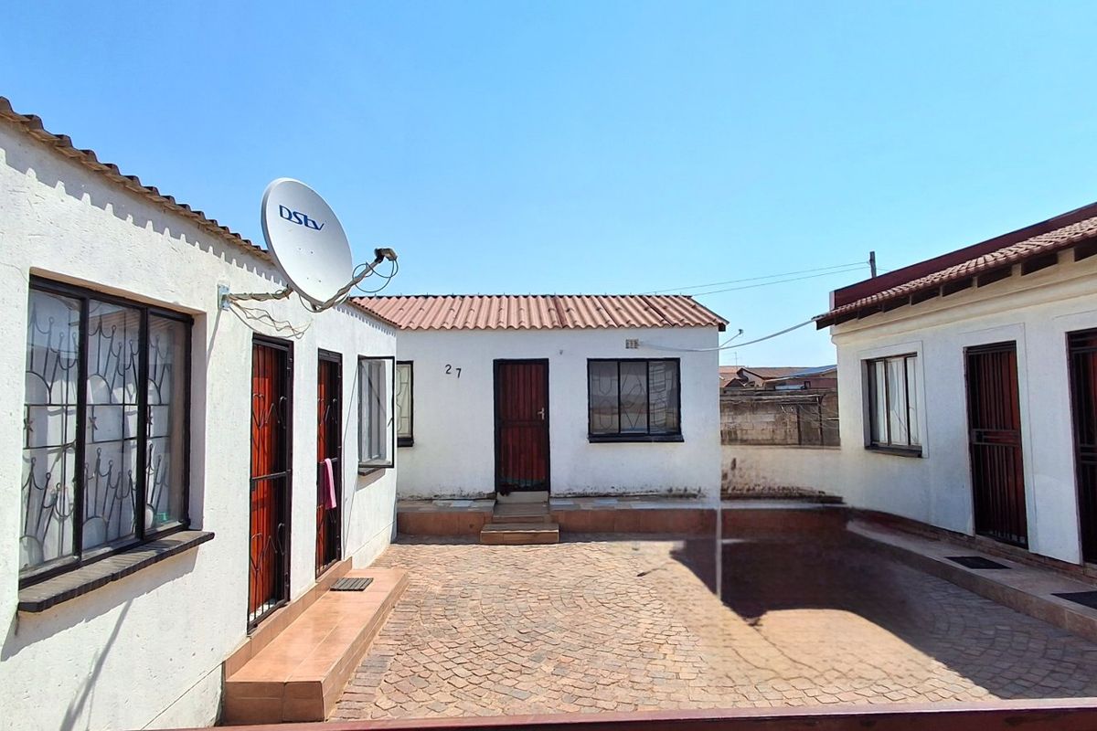 A paved rear courtyard area surrounded by multiple building sections with security gates and tiled roofing.