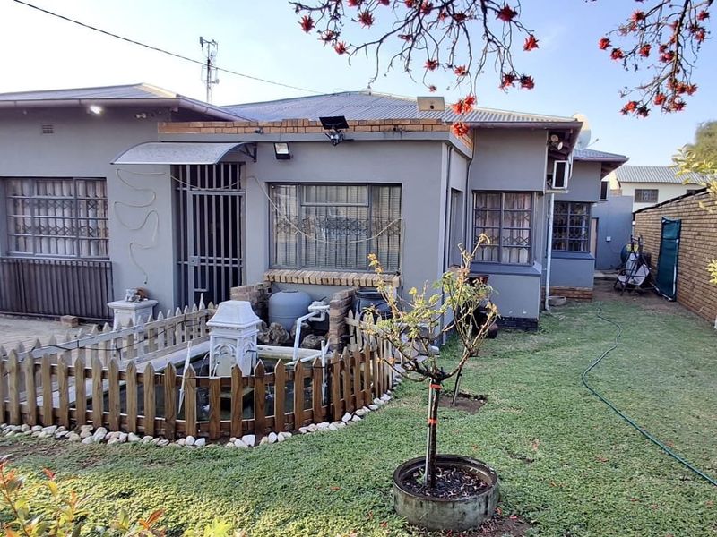 Rear view of the property featuring a paved area, a small water feature, and a landscaped garden with a brick boundary wall.