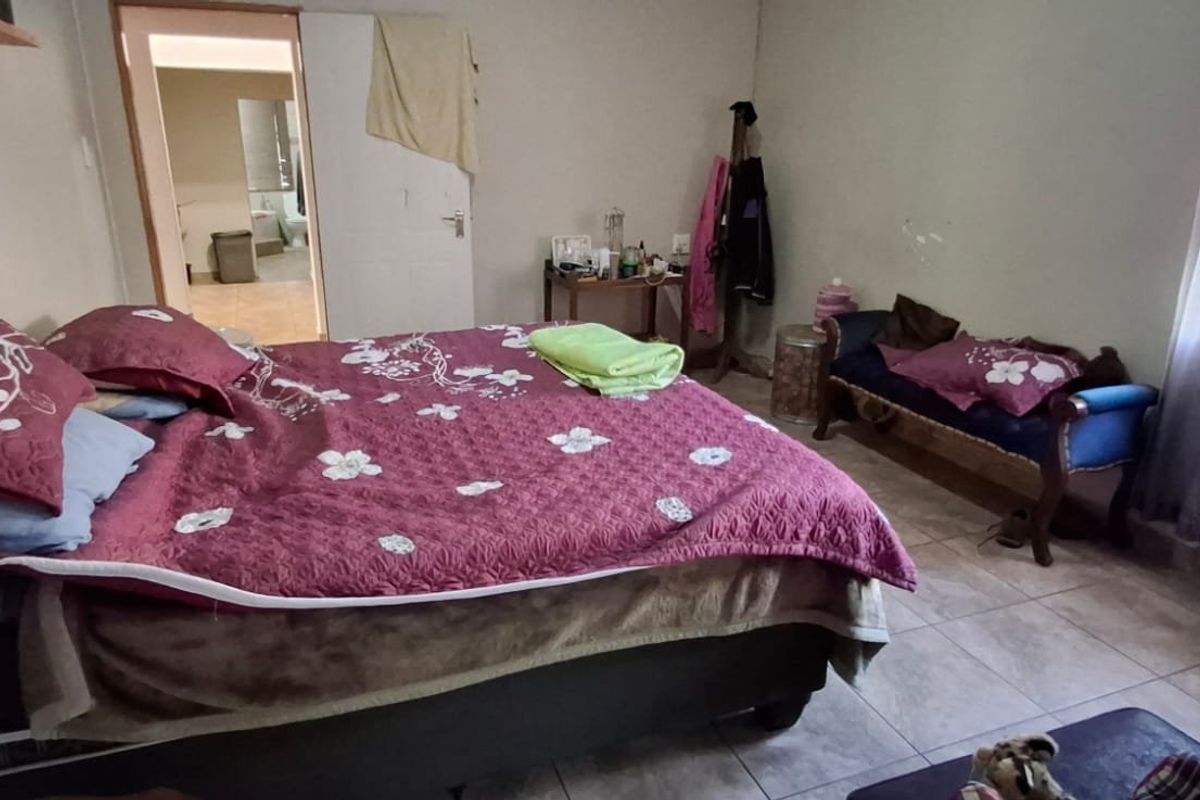 A bedroom featuring tiled flooring and a window with security bars, showing signs of wear on the wall surfaces.