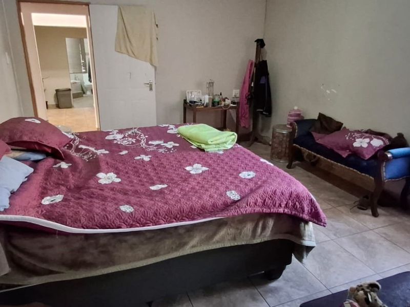 A bedroom featuring tiled flooring and a window with security bars, showing signs of wear on the wall surfaces.