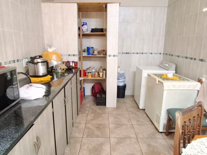 A functional scullery area featuring tiled walls, granite countertops, built-in cabinetry, and dedicated space for laundry appliances.