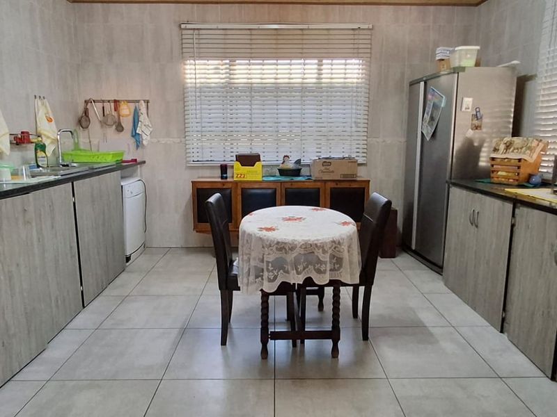 A functional kitchen featuring built-in cabinetry, granite countertops, tiled flooring, and large windows with venetian blinds.