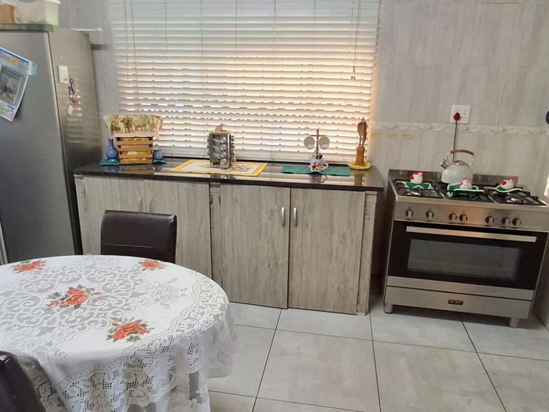 A functional kitchen featuring tiled walls and flooring, built-in cabinetry with stone countertops, and a freestanding gas oven and hob.