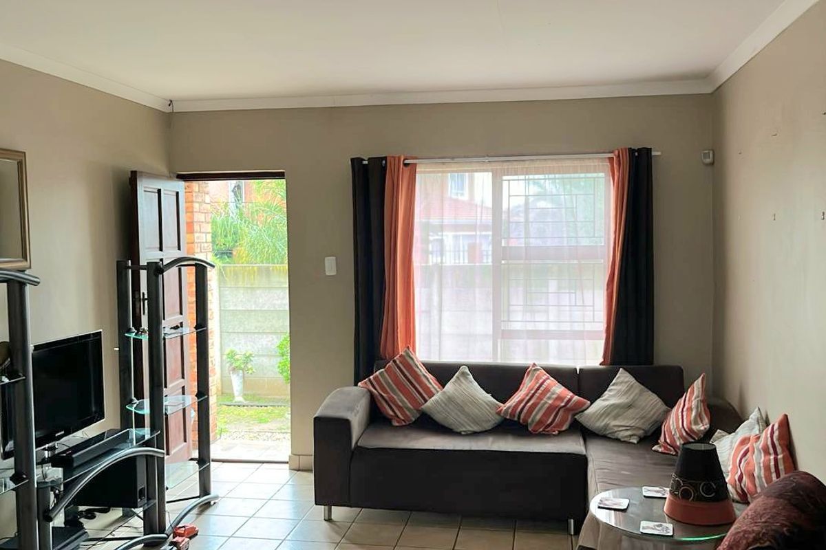 A functional living room featuring tiled flooring, a large window with security bars, and direct access to an outdoor area through a sliding door.