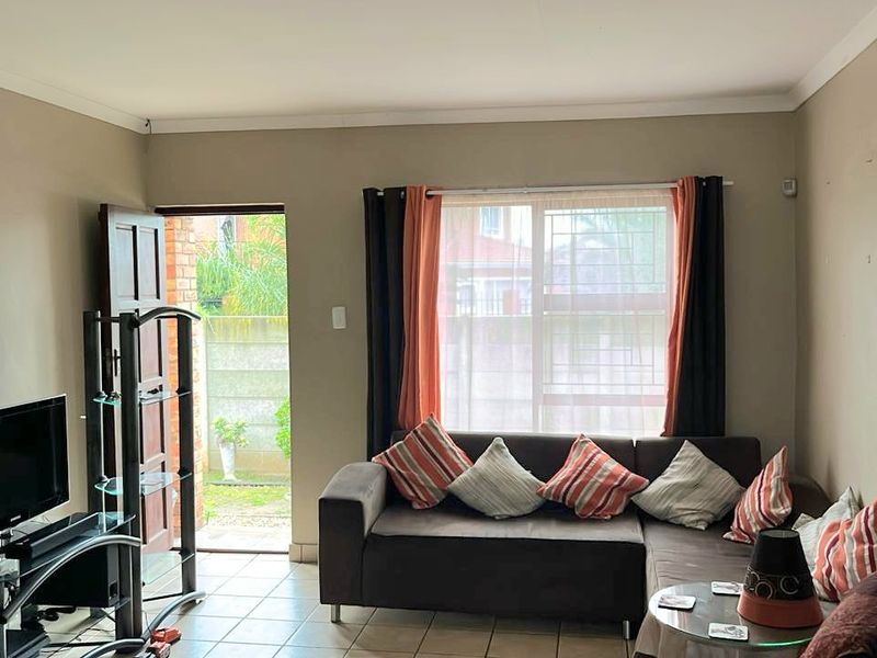 A functional living room featuring tiled flooring, a large window with security bars, and direct access to an outdoor area through a sliding door.