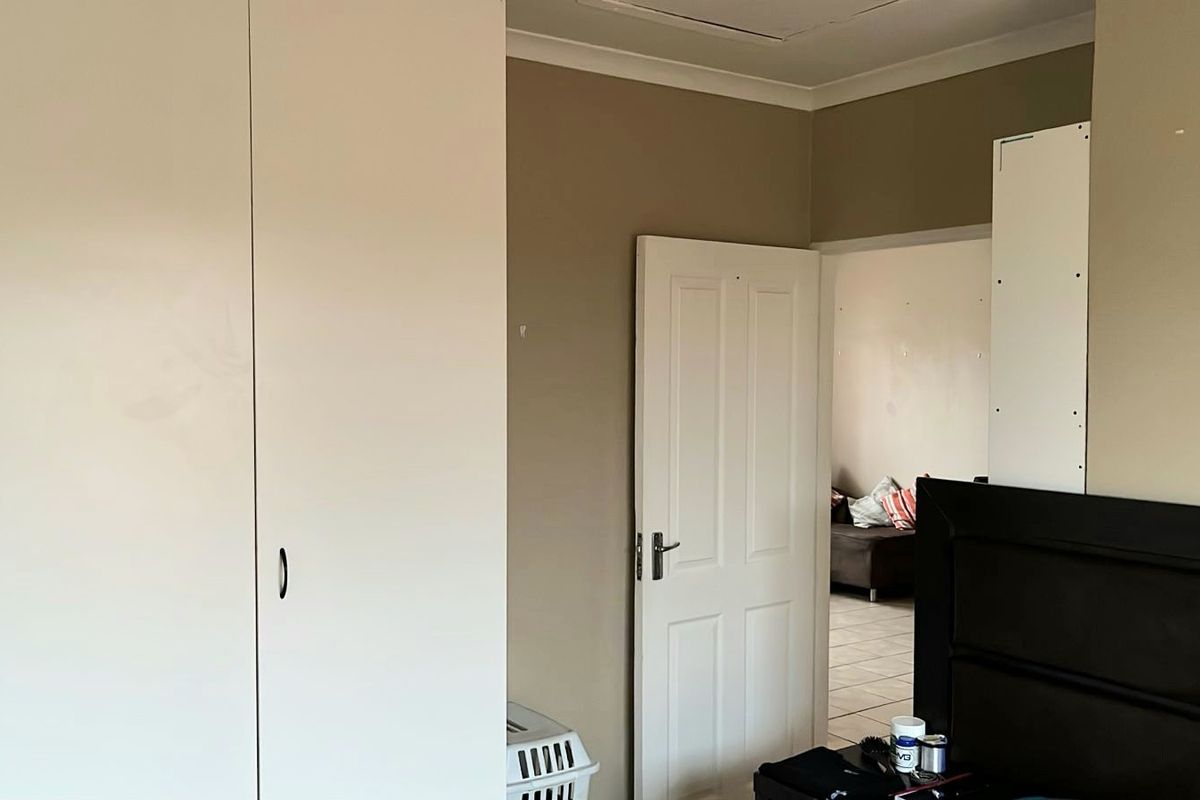 A bedroom featuring built-in white cupboards and neutral wall tones, with a doorway leading to an adjacent living area.