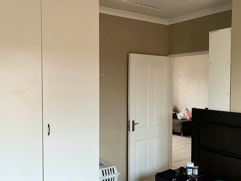 A bedroom featuring built-in white cupboards and neutral wall tones, with a doorway leading to an adjacent living area.