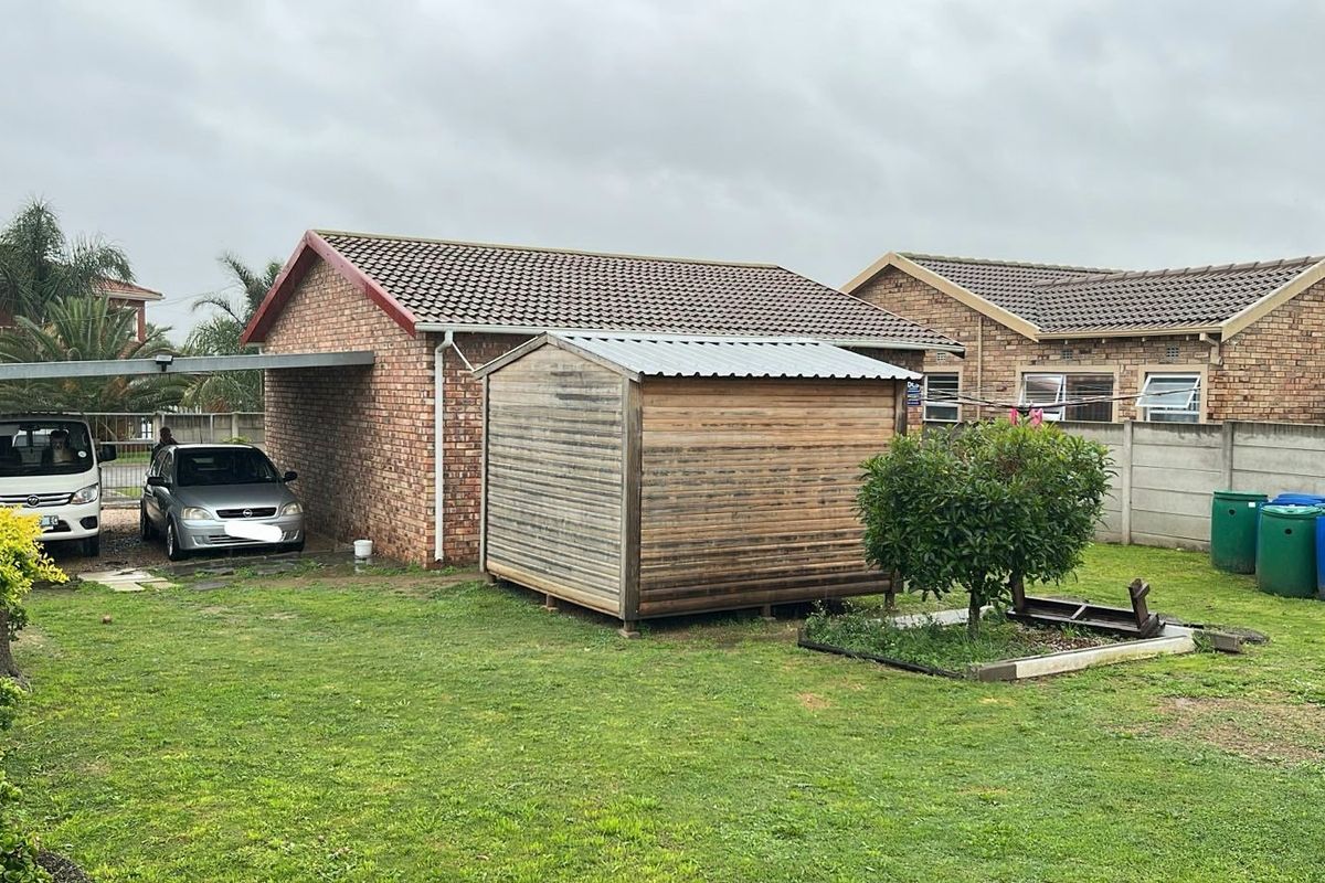 Rear view of the property featuring a brick exterior, tiled roof, attached carport, and a detached timber garden shed set within a grassed yard.