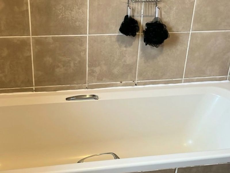 A functional bathroom featuring a standard bathtub with tiled surround and neutral ceramic wall and floor finishes.