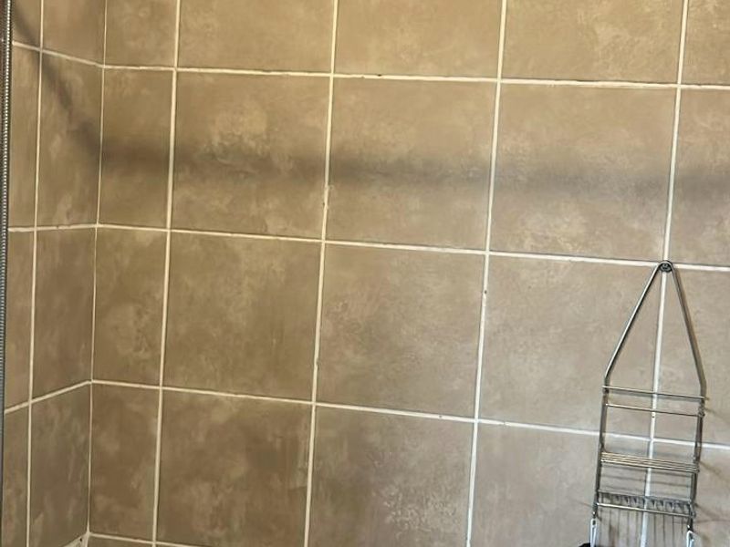 A bathroom shower area featuring beige wall tiles, a standard bathtub, and chrome fixtures, currently showing signs of wear and dated finishes.