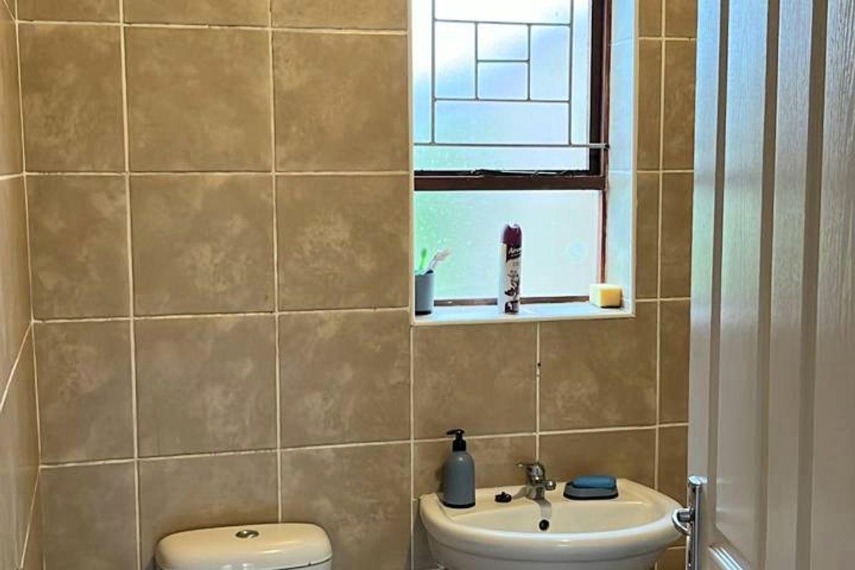 A functional guest bathroom featuring tiled walls, a pedestal basin, and a toilet with a leaded glass window.