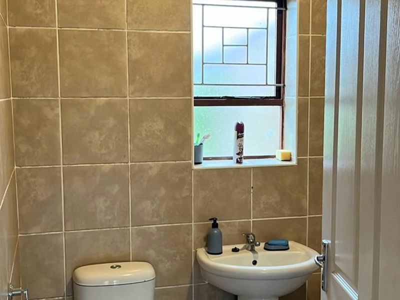 A functional guest bathroom featuring tiled walls, a pedestal basin, and a toilet with a leaded glass window.