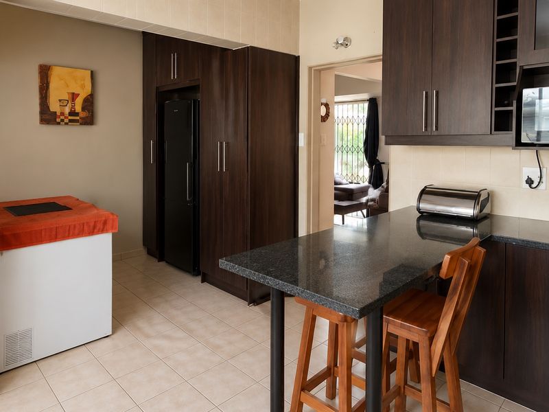 A functional kitchen featuring dark wood cabinetry, granite countertops, a breakfast bar, and tiled flooring, offering a clean and practical workspace.