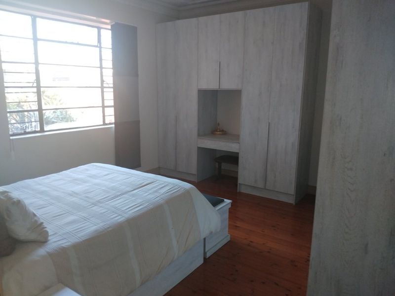 A bedroom featuring timber flooring, a large steel-framed window, and extensive built-in cupboards with an integrated vanity area.