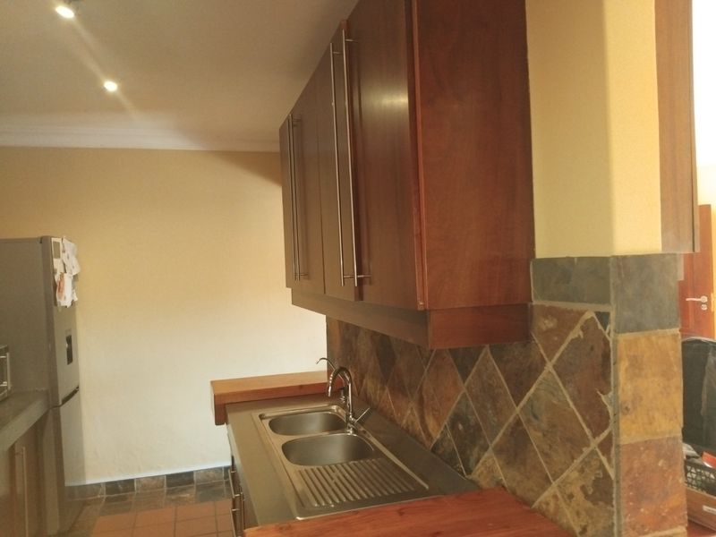A functional kitchen area featuring dark wood cabinetry, stainless steel double sink, slate tile backsplash, and warm wooden countertops.