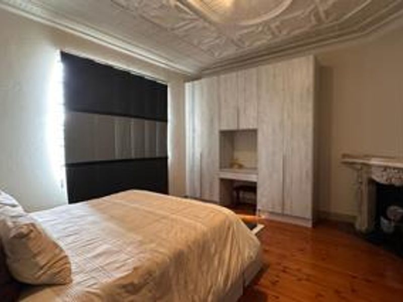 A well-maintained bedroom featuring original ornate ceiling details, polished timber flooring, a classic fireplace, and extensive built-in cabinetry with a vanity nook.