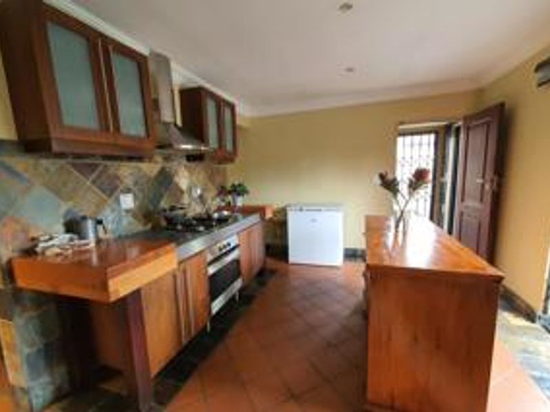 A functional kitchen featuring wooden cabinetry, a built-in oven with gas hob, stone tile backsplash, and a central wooden island with terracotta flooring.
