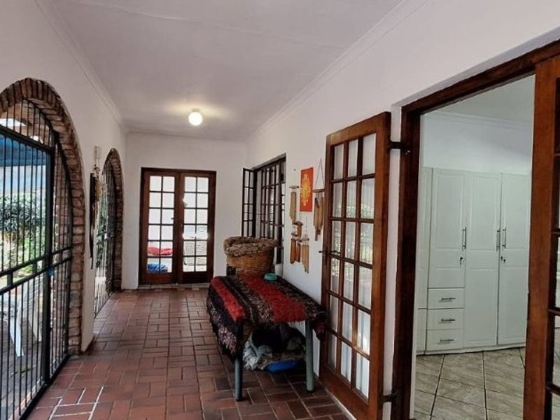 A covered patio area featuring brick flooring, arched brick architectural details, and timber-framed glass doors providing access to the interior.