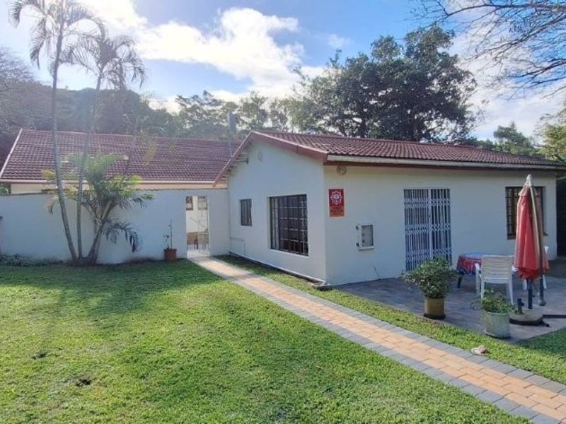 Rear view of the house featuring a paved patio area, built-in braai, and a well-maintained garden setting.