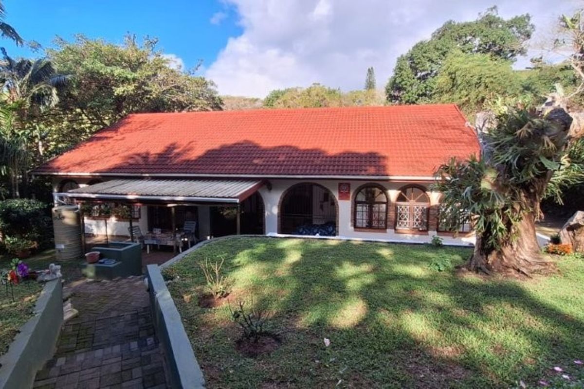 Rear view of the house featuring a terracotta tiled roof, arched windows, and a covered patio overlooking a lush garden.