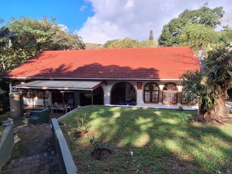 Rear view of the house featuring a terracotta tiled roof, arched windows, and a covered patio overlooking a lush garden.