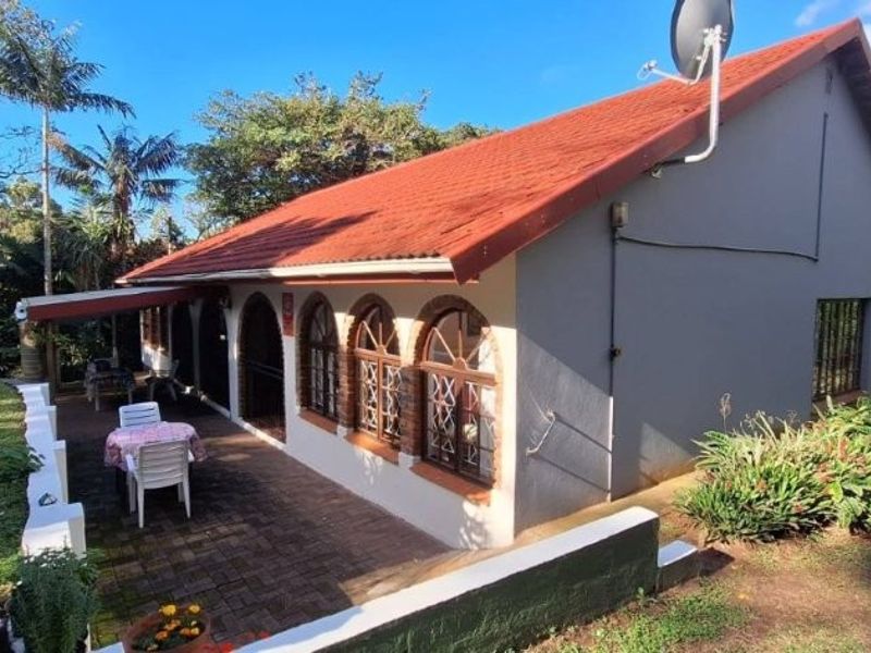 Rear view of the house featuring a covered brick-paved patio, arched windows, and a pitched tiled roof set within a garden environment.