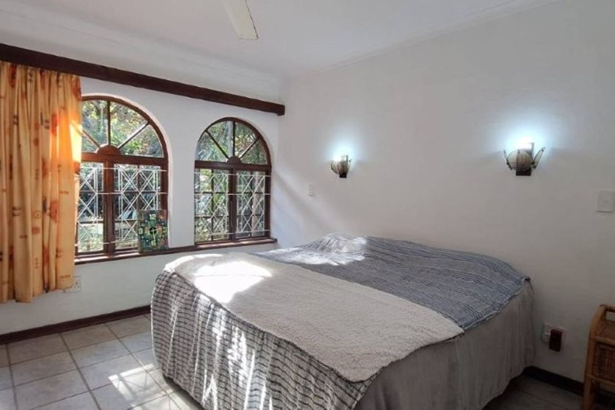 A bedroom featuring arched windows with security bars, tiled flooring, a ceiling fan, and wall-mounted lighting.