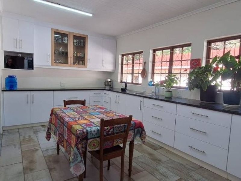 A bright, functional kitchen featuring white cabinetry, dark countertops, and tiled flooring, offering ample storage and workspace with natural light from multiple windows.