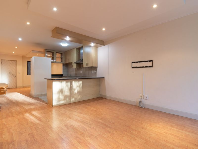 An open-plan living and kitchen area featuring laminate flooring, recessed lighting, and a functional kitchen with built-in cabinetry and a breakfast bar.