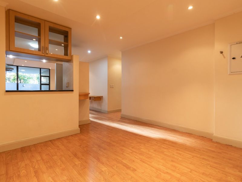 An open-plan living area featuring laminate flooring, recessed downlighting, and a convenient pass-through window connecting to the kitchen space.