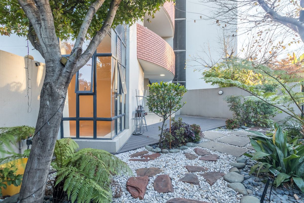 A well-maintained rear garden area featuring stone paving, decking, and a modern building facade with large glass windows.