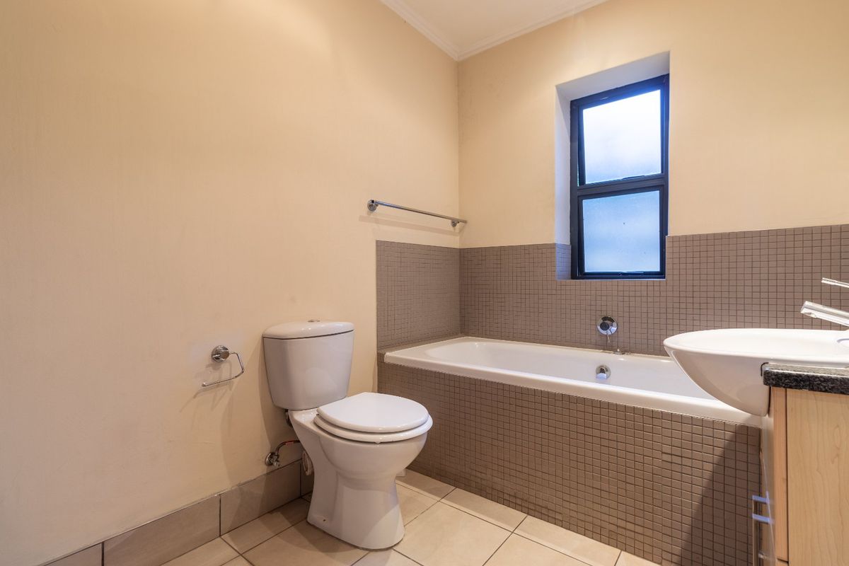 A functional bathroom featuring a bathtub with tiled surround, a pedestal-style vanity with basin, and a toilet, finished with neutral wall paint and floor tiles.