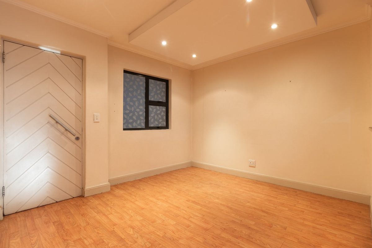 A bright, empty bedroom featuring laminate flooring, a unique chevron-patterned door, and a modern dropped ceiling with recessed lighting.