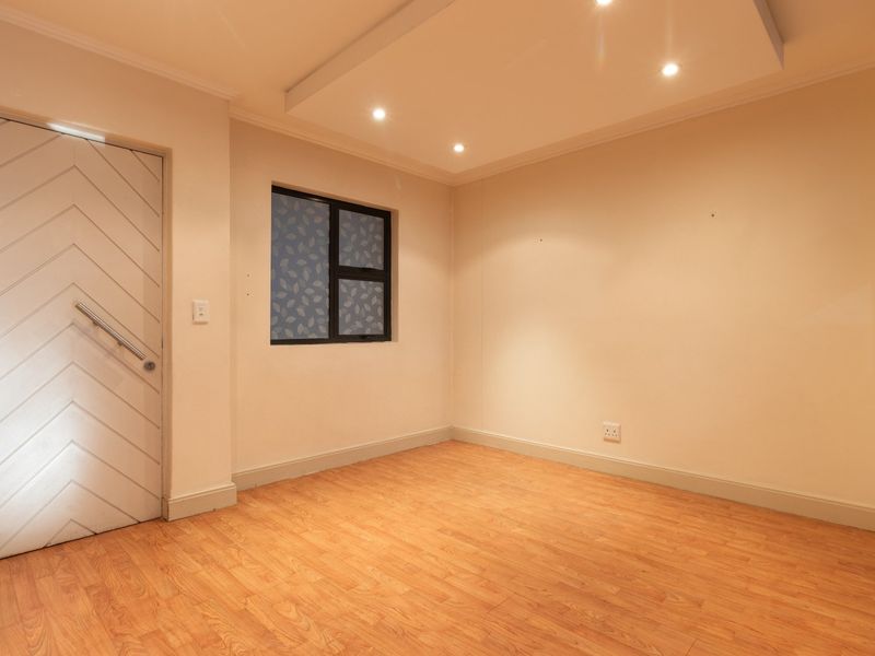 A bright, empty bedroom featuring laminate flooring, a unique chevron-patterned door, and a modern dropped ceiling with recessed lighting.